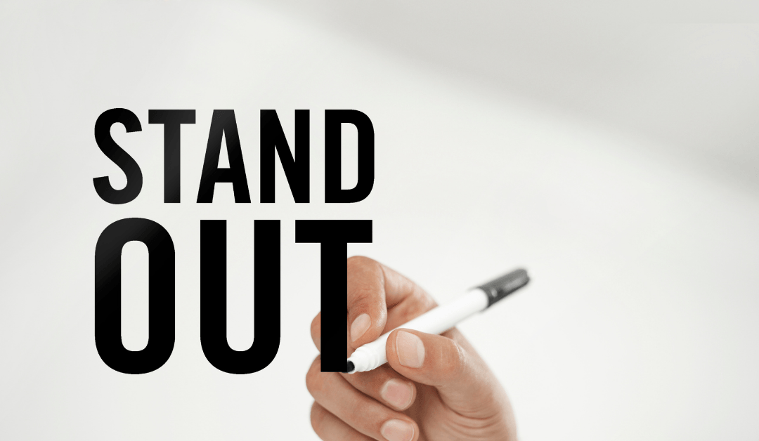 A hand with a pen writing Stand Out.